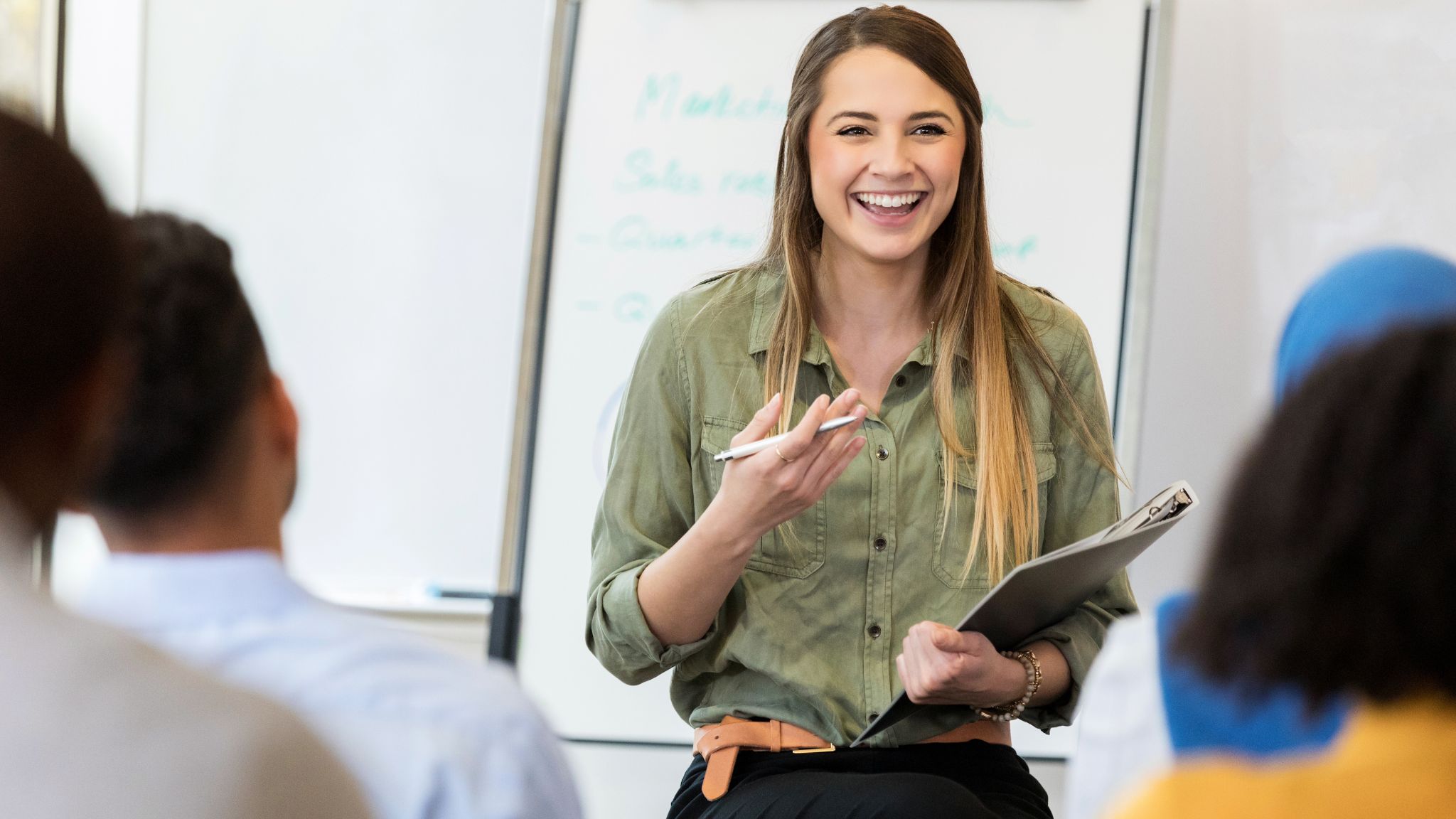 a teacher smiling and talking to students in a classroom.