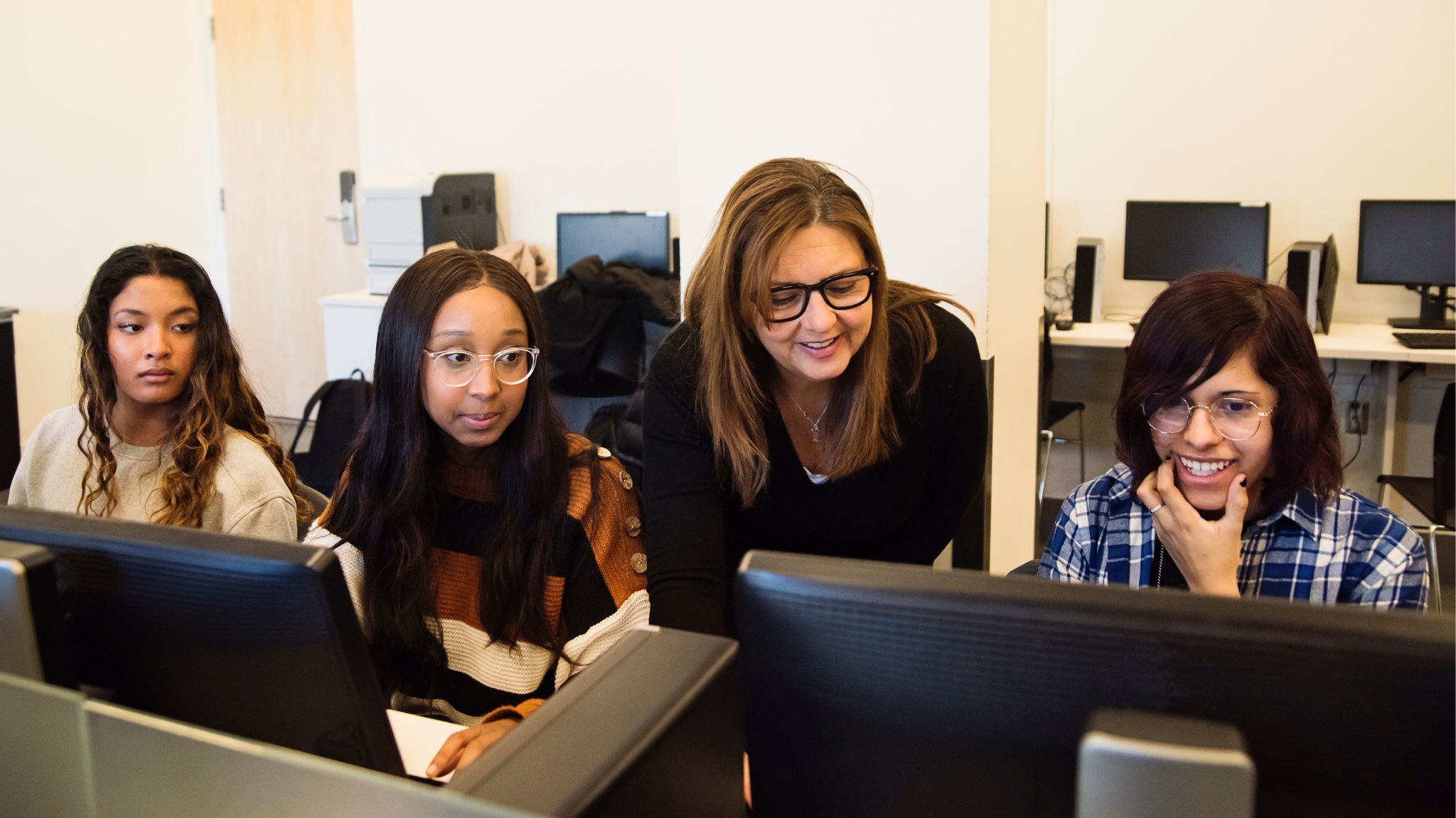 a teacher leaning over to help a student on his computer.