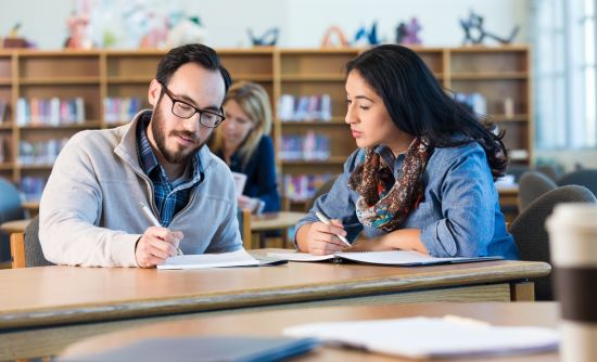 two adult students taking notes in a library.