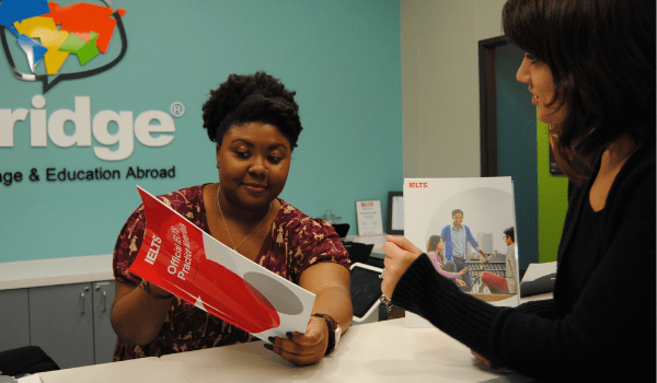 A student speaking with the receptionist about the IELTS test prep course at Bridge in Denver, CO.